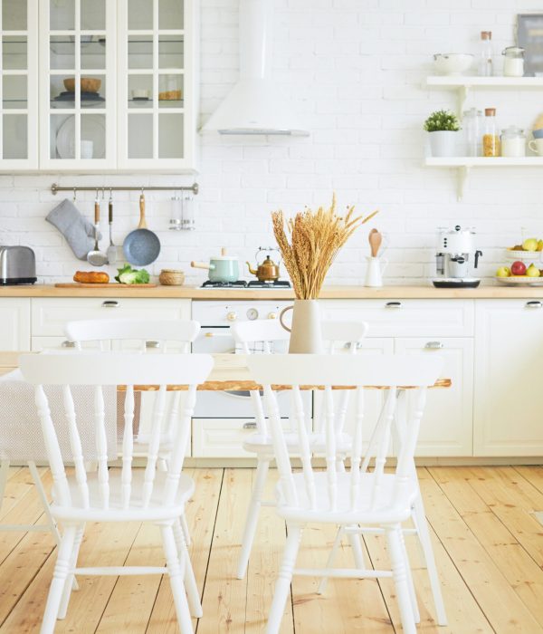 Stylish Scandinavian kitchen interior: chairs and table in foreground, fridge, long wooden counter with machines, utensils on shelves in background. Interiors, design, ideas, home and coziness concept